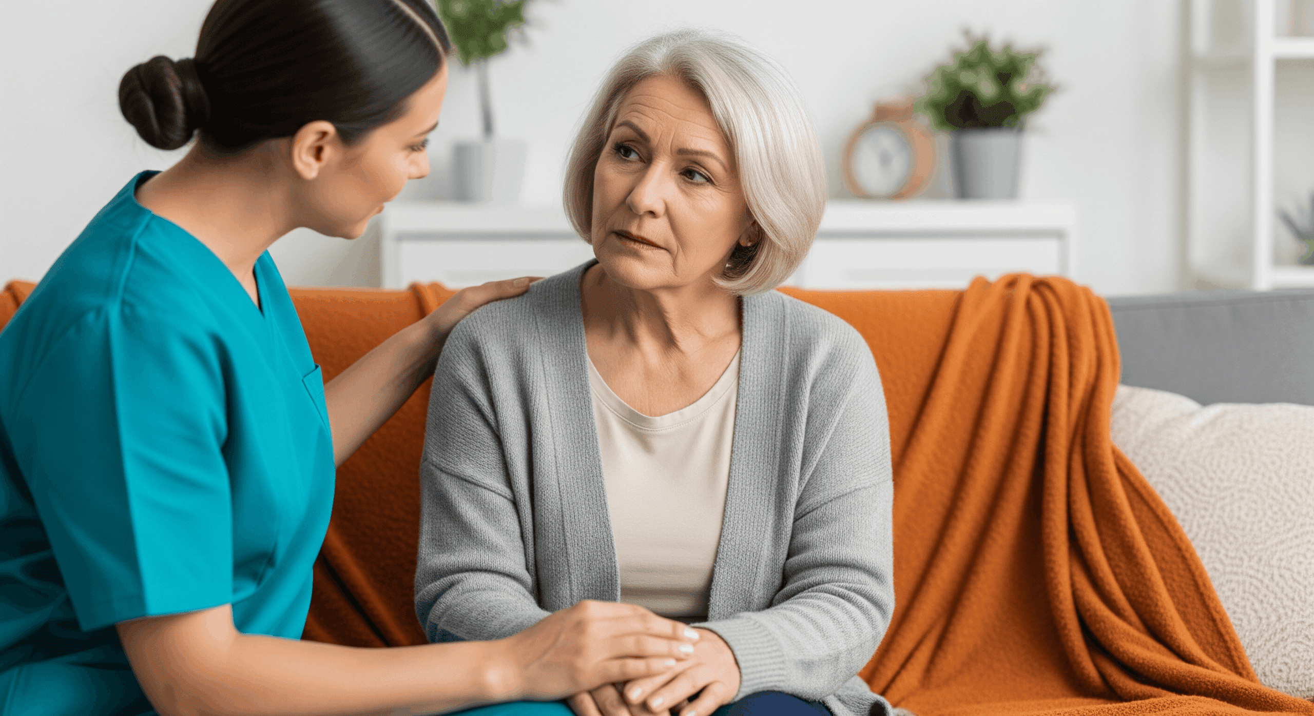 Caregiver sitting beside elderly woman on couch offering comfort and support